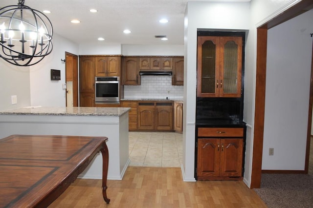 kitchen with an inviting chandelier, light stone counters, kitchen peninsula, oven, and pendant lighting