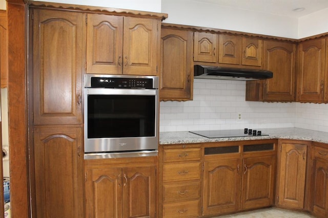 kitchen featuring light stone countertops, decorative backsplash, black electric cooktop, and stainless steel oven