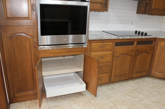 kitchen with decorative backsplash, light stone counters, black electric stovetop, and oven