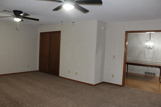 carpeted empty room featuring ceiling fan with notable chandelier and a textured ceiling