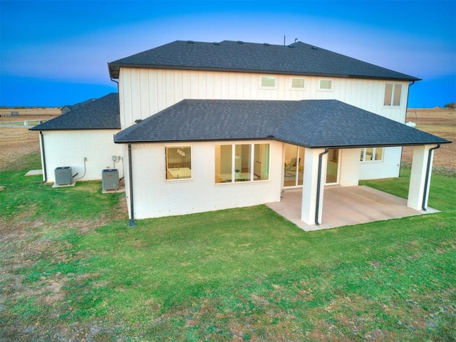 back house at dusk with a patio area, a yard, and central AC