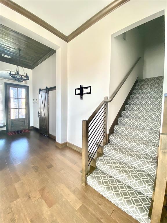 stairway with a barn door, a chandelier, ornamental molding, and hardwood / wood-style flooring