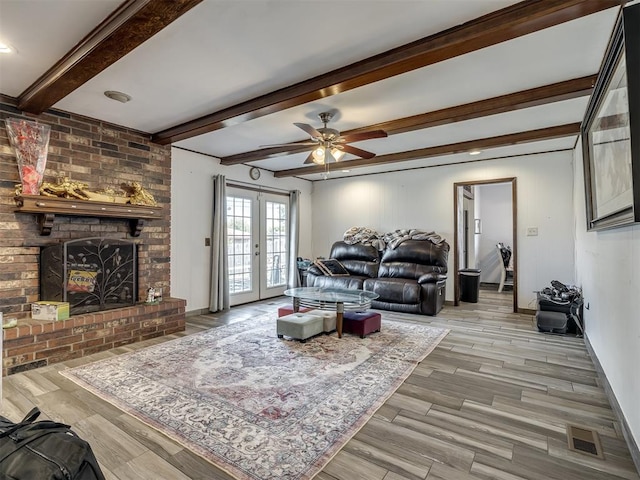 living room featuring french doors, a brick fireplace, ceiling fan, light hardwood / wood-style flooring, and beamed ceiling