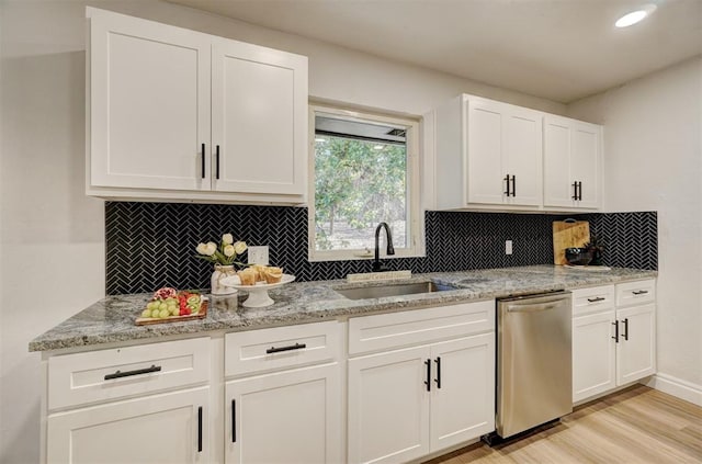 kitchen with backsplash, sink, light hardwood / wood-style flooring, stainless steel dishwasher, and white cabinetry