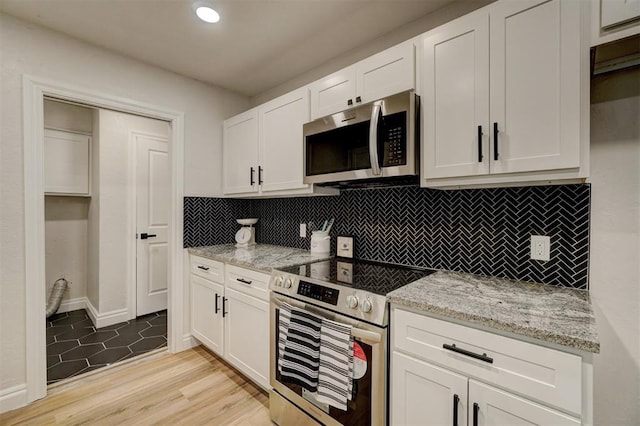 kitchen featuring light stone countertops, tasteful backsplash, appliances with stainless steel finishes, white cabinets, and light wood-type flooring