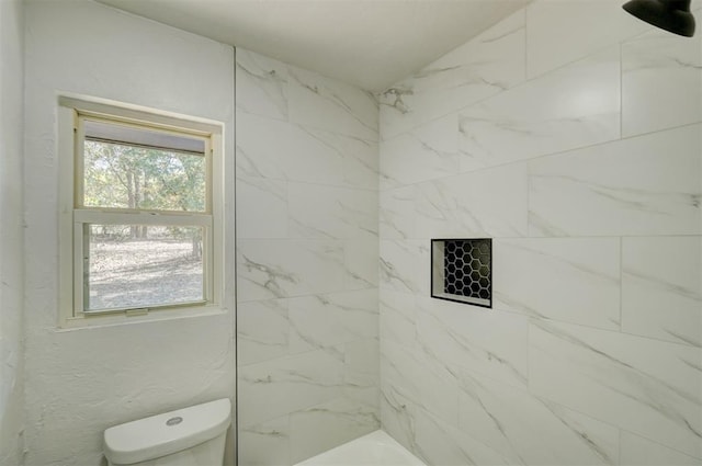 bathroom with a tile shower and toilet