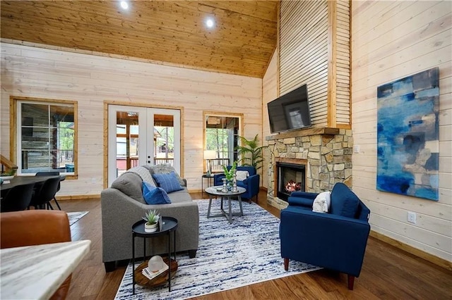 living room featuring french doors, a stone fireplace, high vaulted ceiling, wood-type flooring, and wooden walls