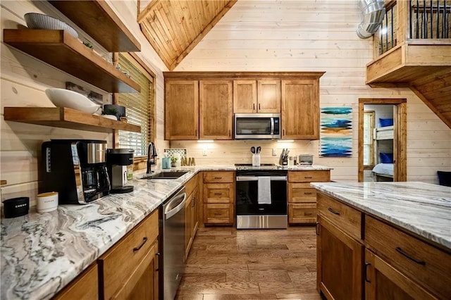 kitchen with appliances with stainless steel finishes, light stone counters, vaulted ceiling, sink, and wood walls