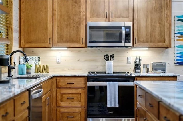 kitchen with backsplash, light stone countertops, sink, and appliances with stainless steel finishes