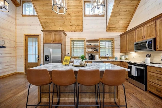 kitchen with a center island, pendant lighting, stainless steel appliances, and wood walls