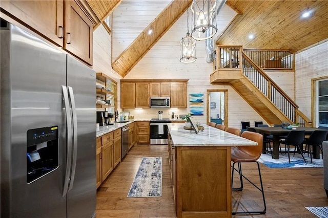 kitchen featuring stainless steel appliances, decorative light fixtures, high vaulted ceiling, wood walls, and a kitchen island