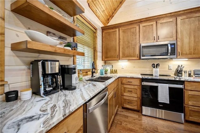 kitchen with appliances with stainless steel finishes, light wood-type flooring, light stone countertops, vaulted ceiling, and sink