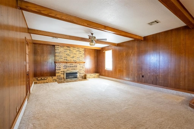 unfurnished living room with wood walls, a brick fireplace, a textured ceiling, light carpet, and beamed ceiling