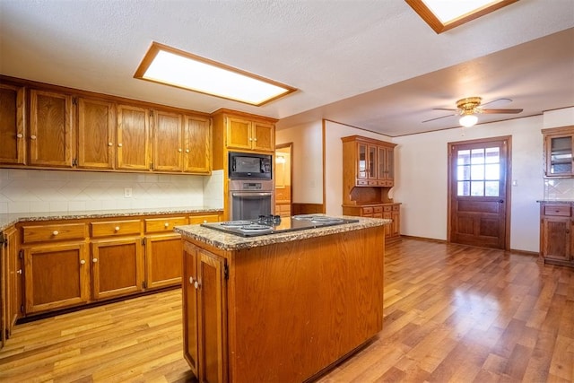 kitchen with tasteful backsplash, light hardwood / wood-style flooring, black appliances, and a center island