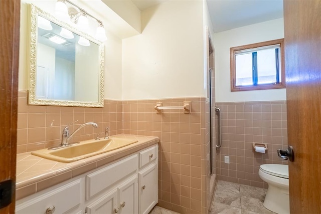 bathroom with toilet, a shower with shower door, tile walls, vanity, and tile patterned flooring