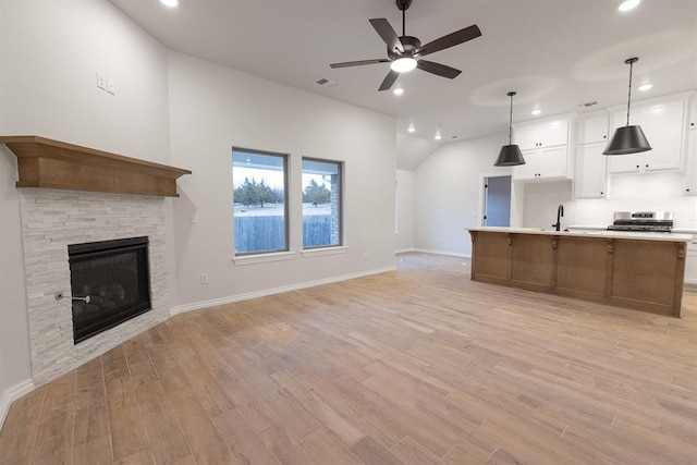 kitchen with light wood finished floors, open floor plan, a fireplace, white cabinetry, and a sink