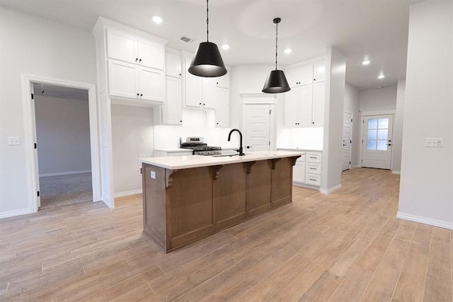 kitchen featuring light countertops, a center island with sink, white cabinetry, and light wood-style floors