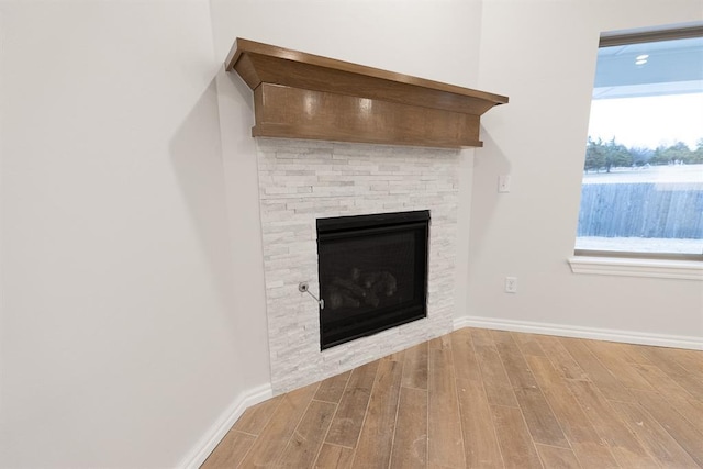 interior details featuring a stone fireplace, wood finished floors, and baseboards