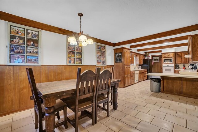 dining space featuring wooden walls, sink, beamed ceiling, and an inviting chandelier