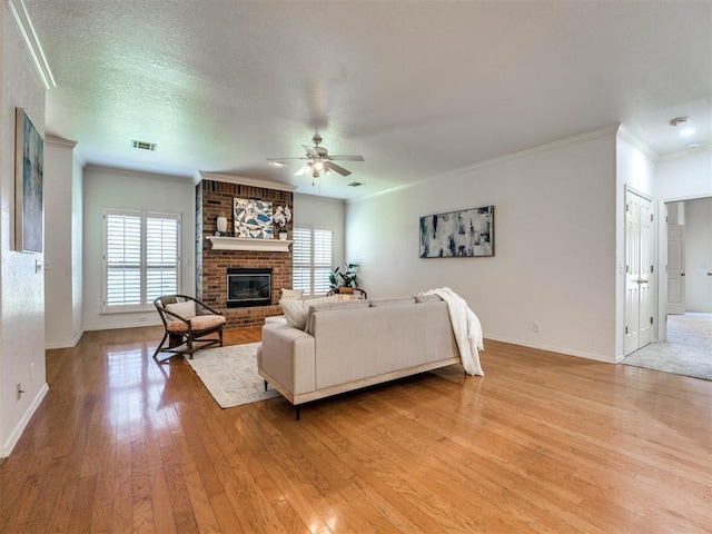 living room featuring a brick fireplace, light hardwood / wood-style flooring, ceiling fan, ornamental molding, and a textured ceiling