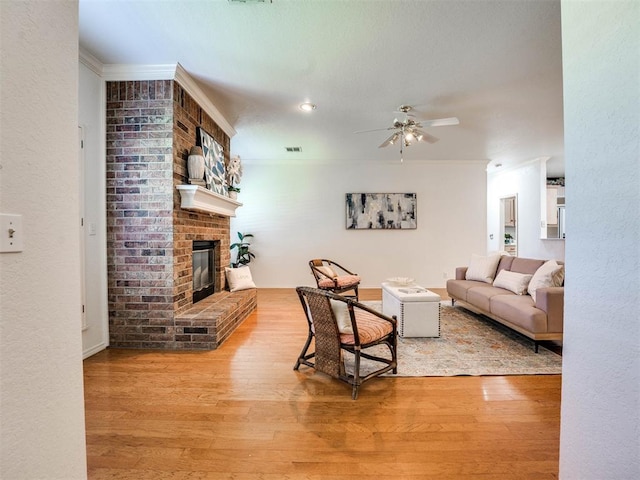 living room featuring ceiling fan, crown molding, wood-type flooring, and a brick fireplace