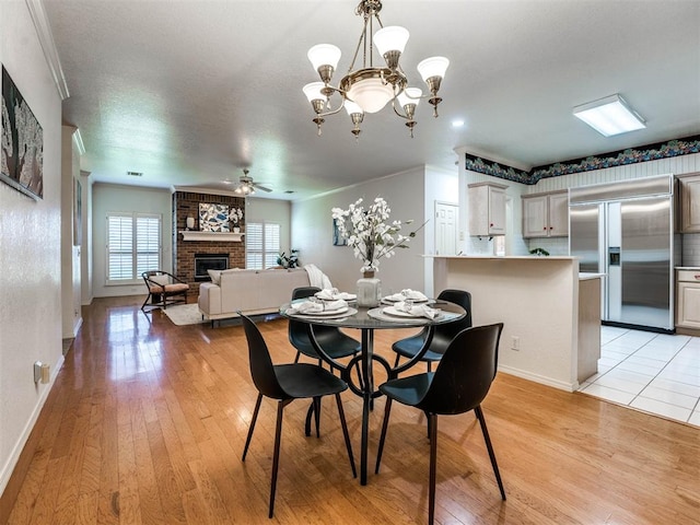 dining room with ceiling fan with notable chandelier, light hardwood / wood-style floors, ornamental molding, and a fireplace