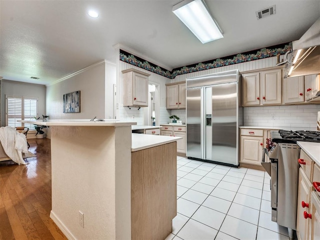 kitchen with kitchen peninsula, light wood-type flooring, backsplash, stainless steel appliances, and light brown cabinets