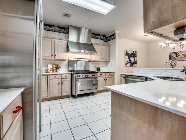 kitchen with sink, stainless steel appliances, wall chimney range hood, an inviting chandelier, and crown molding