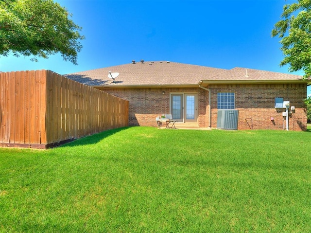 rear view of house featuring central air condition unit, brick siding, fence, french doors, and a lawn