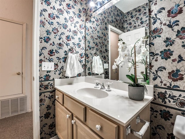 bathroom with visible vents, vanity, and wallpapered walls