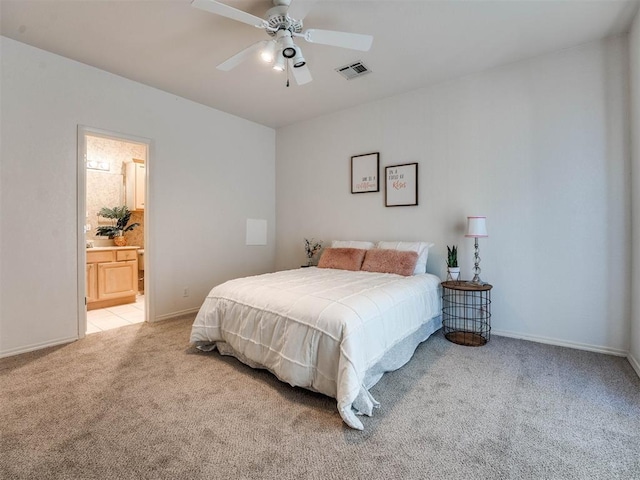 bedroom with ceiling fan, light colored carpet, visible vents, baseboards, and ensuite bath