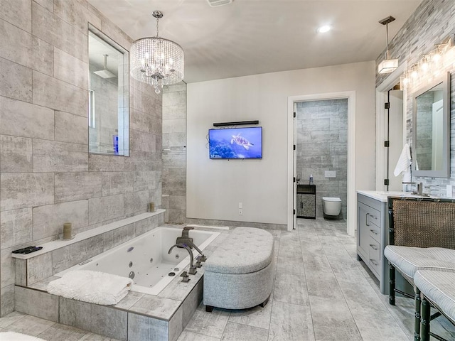 bathroom featuring a relaxing tiled tub, a chandelier, toilet, vanity, and tile walls