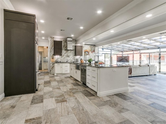 kitchen featuring wall chimney range hood, a kitchen island, backsplash, crown molding, and white cabinets