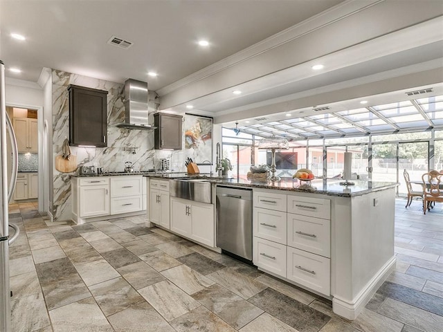 kitchen with a center island, wall chimney exhaust hood, tasteful backsplash, white cabinets, and appliances with stainless steel finishes