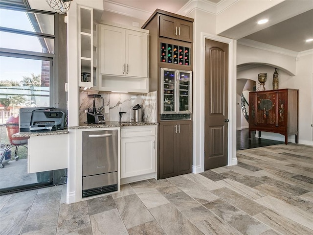 bar featuring backsplash, wine cooler, light stone countertops, ornamental molding, and white cabinetry