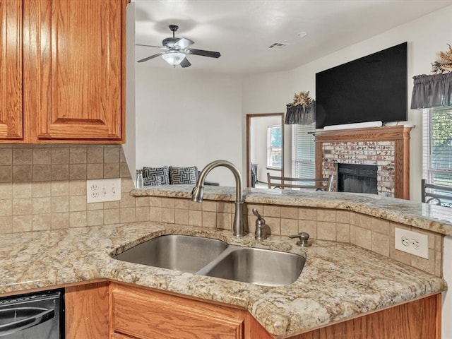 kitchen featuring sink, a brick fireplace, stainless steel dishwasher, ceiling fan, and light stone counters