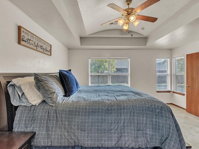 bedroom with ceiling fan, a raised ceiling, carpet floors, and multiple windows