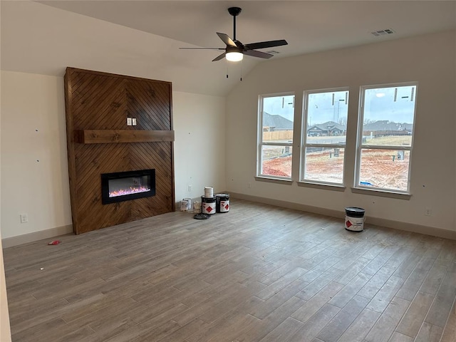 unfurnished living room with ceiling fan, a large fireplace, vaulted ceiling, and light hardwood / wood-style flooring