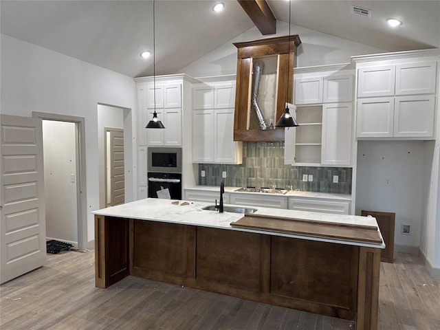 kitchen with lofted ceiling with beams, hardwood / wood-style flooring, an island with sink, appliances with stainless steel finishes, and white cabinetry