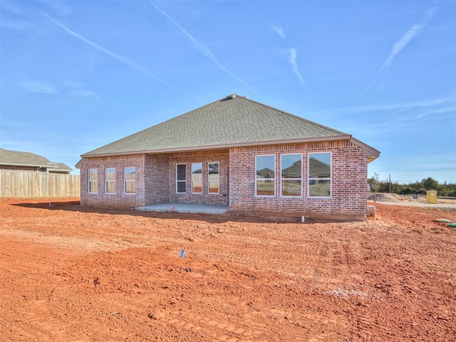 rear view of house featuring a patio area, roof with shingles, fence, and brick siding