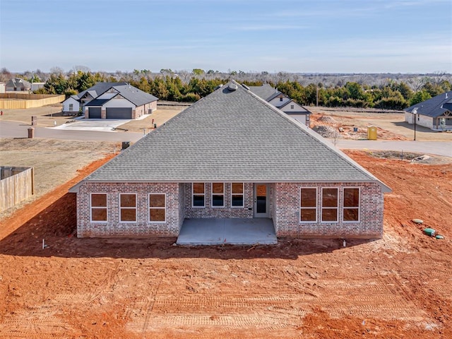 exterior space featuring a patio area, fence, brick siding, and roof with shingles