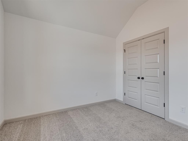 unfurnished room with lofted ceiling, baseboards, and light colored carpet