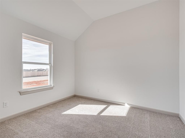 spare room featuring lofted ceiling, light colored carpet, and baseboards