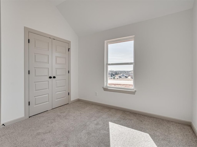 unfurnished bedroom featuring lofted ceiling, a closet, carpet flooring, and baseboards