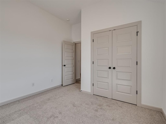 unfurnished bedroom with a closet, light colored carpet, and baseboards