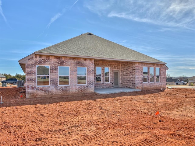 back of property with brick siding, roof with shingles, and a patio area