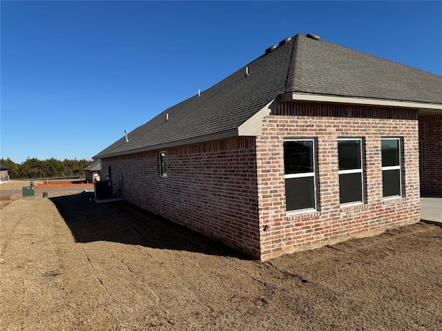 view of home's exterior with brick siding and a shingled roof