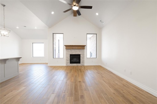 unfurnished living room with baseboards, a fireplace, light wood-style floors, visible vents, and ceiling fan with notable chandelier