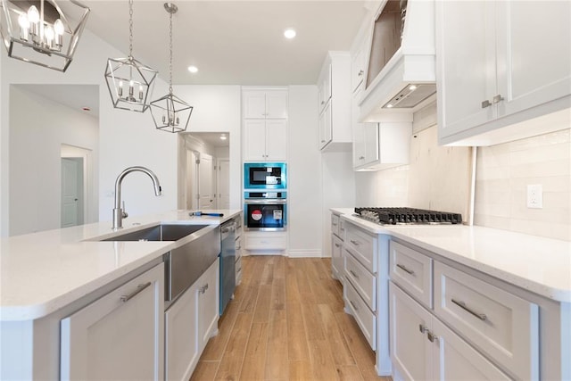 kitchen with an inviting chandelier, tasteful backsplash, white cabinetry, custom exhaust hood, and stainless steel appliances