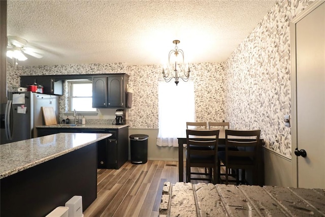 kitchen with sink, stainless steel fridge, a textured ceiling, decorative light fixtures, and wood-type flooring